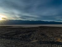 an empty dirt field with a fire hydrant near it and some mountains under a cloudy sky