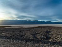 an empty dirt field with a fire hydrant near it and some mountains under a cloudy sky