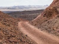 dirt road in an arid area with mountains in the background and a man riding on the back of a mountain bike