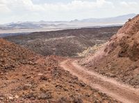 dirt road in an arid area with mountains in the background and a man riding on the back of a mountain bike