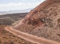 dirt road in an arid area with mountains in the background and a man riding on the back of a mountain bike