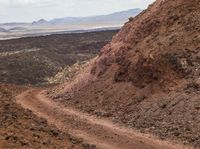 dirt road in an arid area with mountains in the background and a man riding on the back of a mountain bike