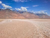 an arid plain with mountains in the background and gravel, rocks and a tiny plane