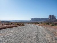 a gravel road runs through a desert landscape with some rocky cliffs and a bright blue sky