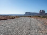 a gravel road runs through a desert landscape with some rocky cliffs and a bright blue sky