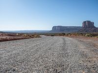 a gravel road runs through a desert landscape with some rocky cliffs and a bright blue sky