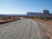 a gravel road runs through a desert landscape with some rocky cliffs and a bright blue sky