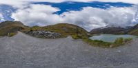 a fish - eye view of a road passing by mountains next to a lake and a forest