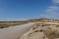 road leading to a small, sandy area with mountains in the background in an arid land