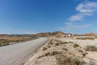 road leading to a small, sandy area with mountains in the background in an arid land