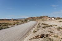 road leading to a small, sandy area with mountains in the background in an arid land