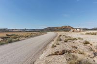 road leading to a small, sandy area with mountains in the background in an arid land