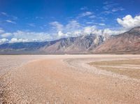 a barren desert is shown with mountains in the background and some clouds in the sky