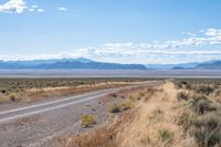 the road is in an empty stretch of dirt with mountains in the distance in the background