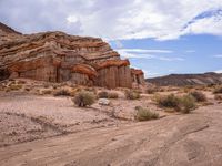 a dirt road passing through the desert next to mountains and rocks that are on top of each other