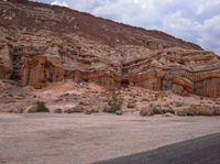 an empty dirt road next to a rocky area with many small bushes and rocks in the foreground