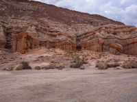 an empty dirt road next to a rocky area with many small bushes and rocks in the foreground