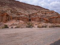 an empty dirt road next to a rocky area with many small bushes and rocks in the foreground