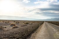 an open road in the desert next to mountains and grass on it during the day