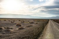 an open road in the desert next to mountains and grass on it during the day