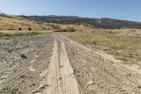 dirt road with two tracks in the middle and hills behind it on the left side