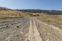 dirt road with two tracks in the middle and hills behind it on the left side