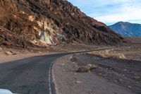 the car is driving along the wide paved road in the desert area, in front of a high mountain