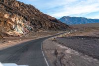 the car is driving along the wide paved road in the desert area, in front of a high mountain