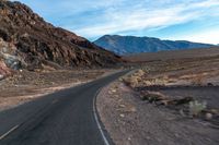 the car is driving along the wide paved road in the desert area, in front of a high mountain