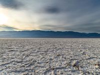 a dirt plain with lots of mountains in the background with a hazy sky overhead and snow