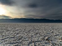 a dirt plain with lots of mountains in the background with a hazy sky overhead and snow