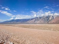 a vast open desert area with mountains in the background and clouds in the distance over the horizon