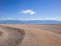 a road in the middle of the desert with mountains and blue sky in the background