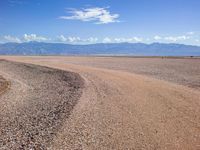 a road in the middle of the desert with mountains and blue sky in the background