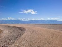 a road in the middle of the desert with mountains and blue sky in the background