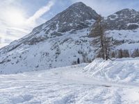 a snow skier is walking towards a snowy mountain, near a small tree line and mountains