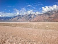 a barren landscape with mountains in the distance and clouds over it, a bright blue sky is visible