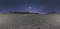 a desert with a few hills at night in the distance of the horizon, and a bright moon above the hills