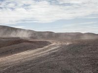 dirt running on top of a mountain next to a trail and some hills with dust rising from it