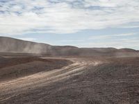 dirt running on top of a mountain next to a trail and some hills with dust rising from it