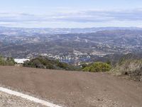 the road runs through a small wooded area by a mountain with a view of town in the distance