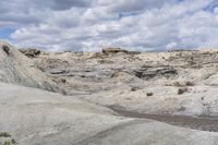 a horse is standing on a dirt hillside near some rocks and water in the distance