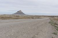 a dirt road near the middle of a barren area with mountains in the distance, while a person rides on an orange motorcycle