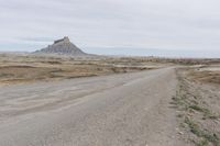 a dirt road near the middle of a barren area with mountains in the distance, while a person rides on an orange motorcycle