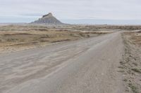 a dirt road near the middle of a barren area with mountains in the distance, while a person rides on an orange motorcycle