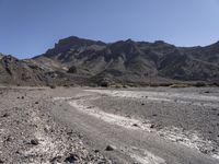 gravel road leading to a mountain that is rocky and dry with mountains in the background