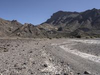 gravel road leading to a mountain that is rocky and dry with mountains in the background