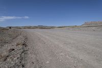 a dirt road is surrounded by some hills and desert like terrain as the vehicle sits on it