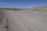 a dirt road is surrounded by some hills and desert like terrain as the vehicle sits on it