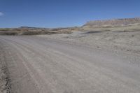 a dirt road is surrounded by some hills and desert like terrain as the vehicle sits on it